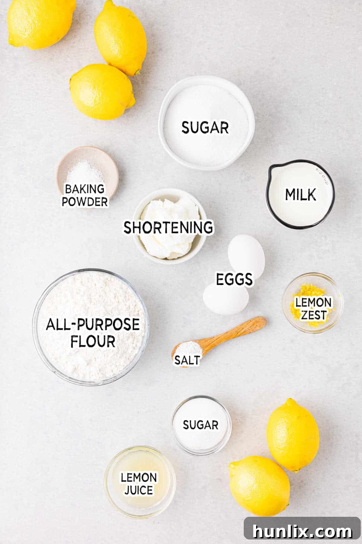 A collection of fresh ingredients laid out for making lemon bread, including lemons, flour, eggs, sugar, and milk.