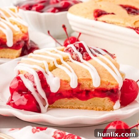 A beautifully glazed slice of cherry cake on a white plate, ready to be enjoyed.