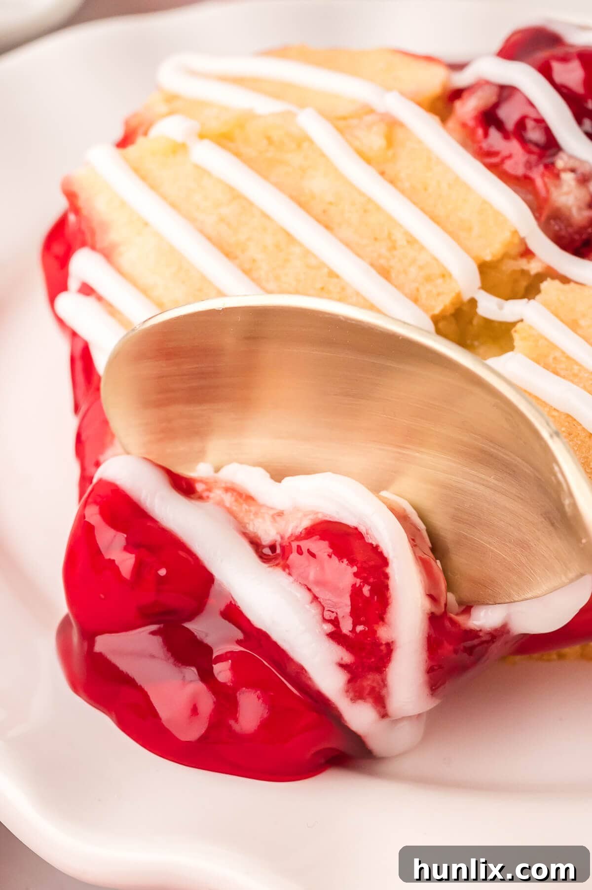 A spoon pushing through a piece of cherry cake, highlighting its soft texture and the juicy cherry layer.