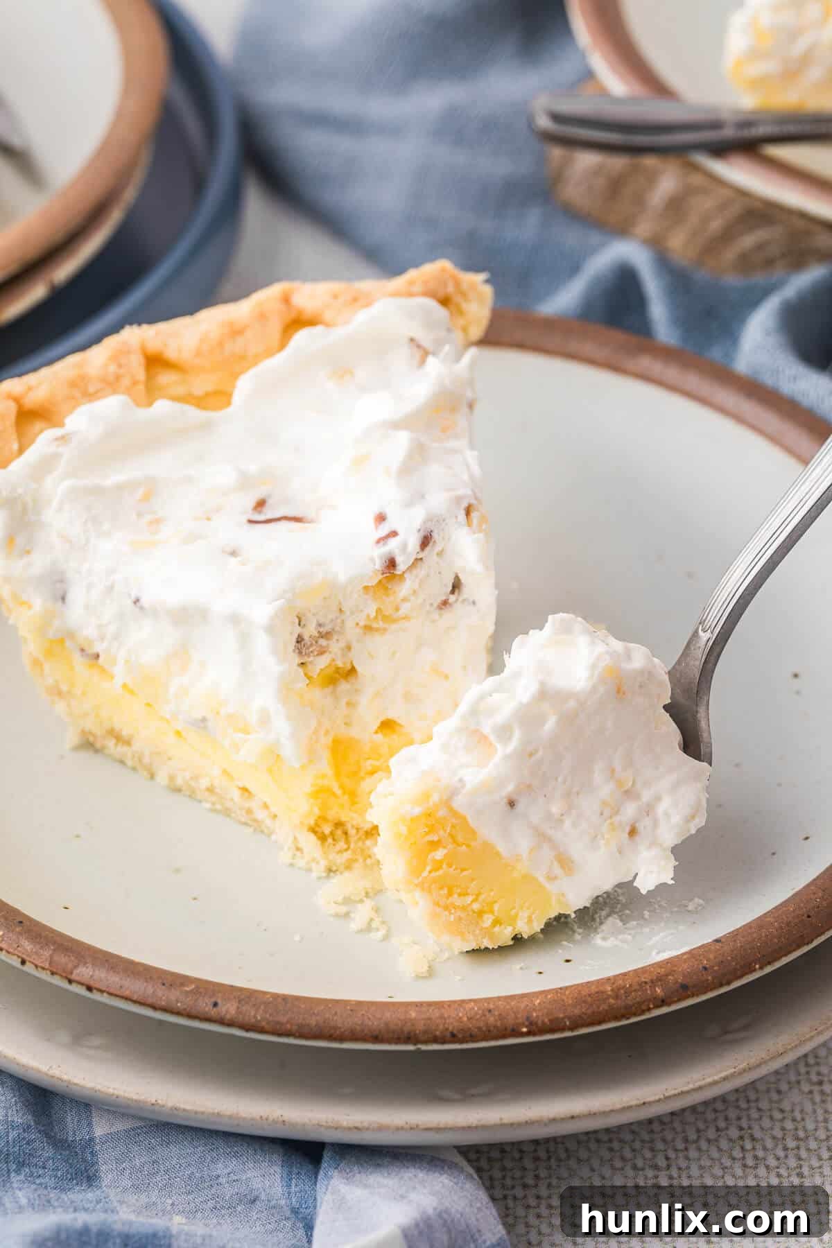 A close-up of a slice of Millionaire Pie on a white plate, with a fork having taken a bite, revealing the rich, creamy interior and pecan pieces.