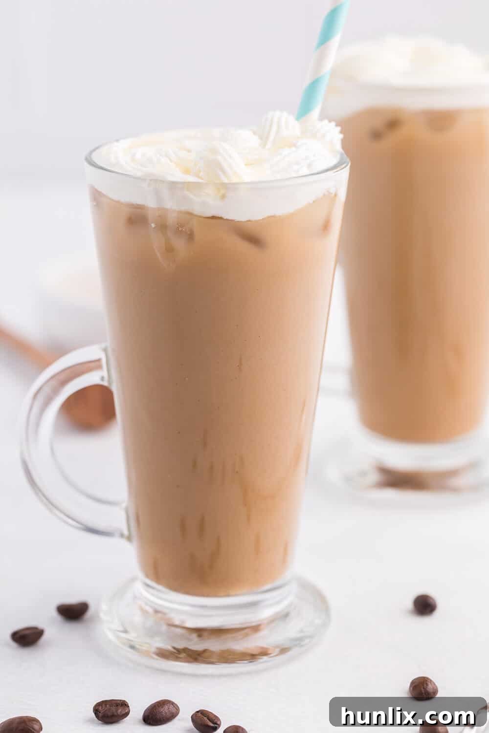 The finished Iced Honey Almond Milk Latte in a clear glass mug, topped with a generous swirl of homemade whipped cream and an enticing drizzle of golden honey.