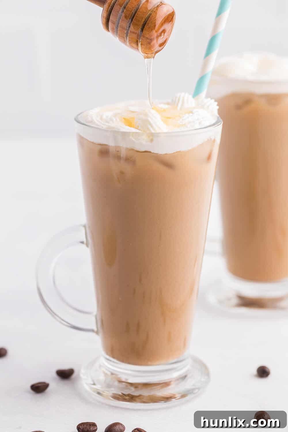 A close-up shot of honey being artfully drizzled onto a mug of Iced Honey Almond Milk Latte, generously topped with fluffy whipped cream, emphasizing the drink's indulgent finish.