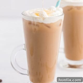 A glass mug of the Iced Honey Almond Milk Latte, beautifully topped with homemade whipped cream and a delicate honey drizzle, ready to be enjoyed.