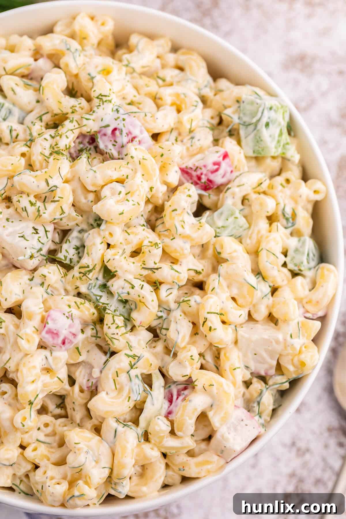 A white bowl of macaroni dill salad garnished with fresh dill.
