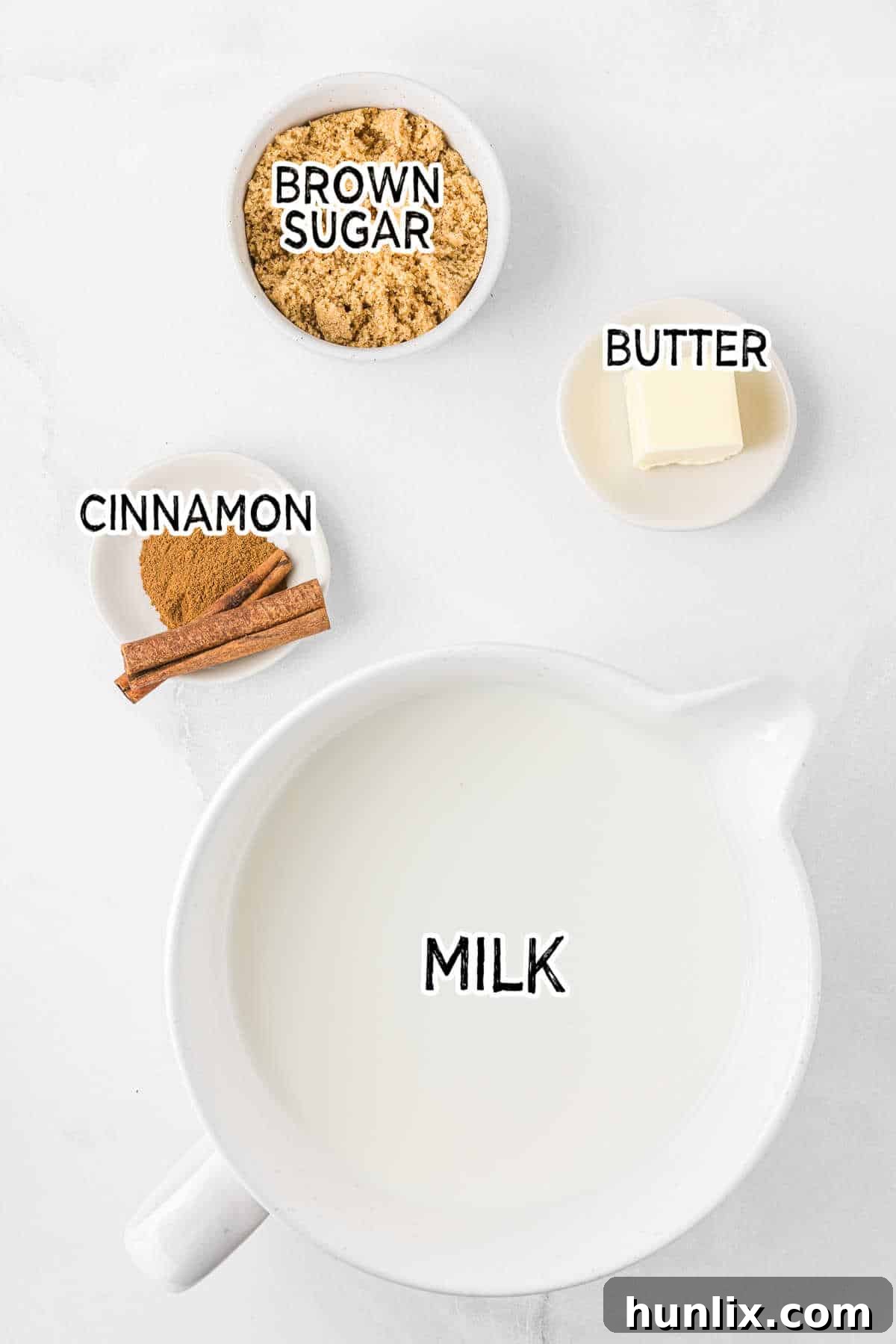 A simple arrangement of ingredients for a butterscotch steamer: milk in a glass, a block of butter, and a bowl of brown sugar, set against a clean white background.