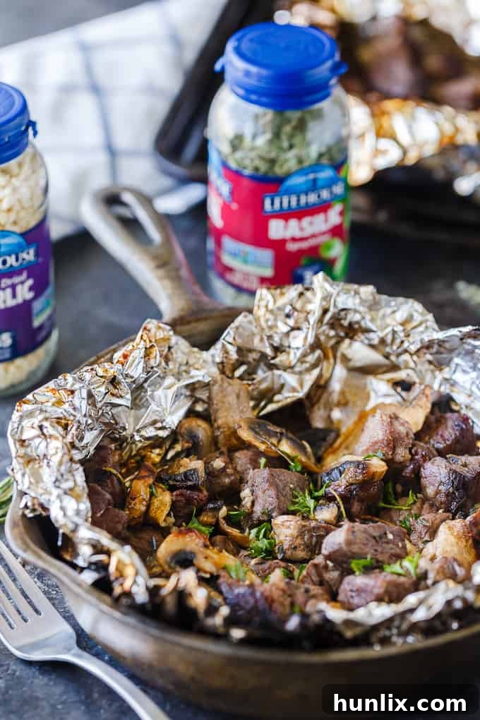 Close-up of freshly cooked Garlic Steak Bites with mushrooms in an individual foil packet, garnished with fresh herbs.