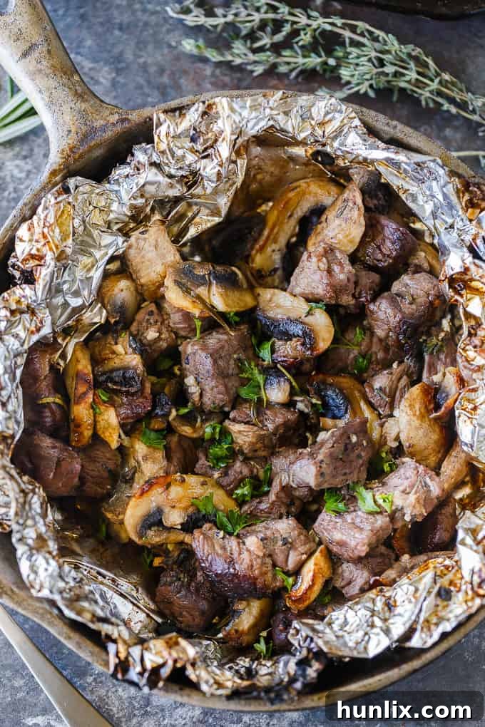 Individual serving of Garlic Steak Bites with melted herb butter, ready to be enjoyed straight from the foil packet.