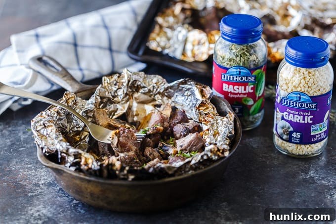 Overhead view of several individual foil packets of Garlic Steak Bites arranged on a platter, ready for serving.