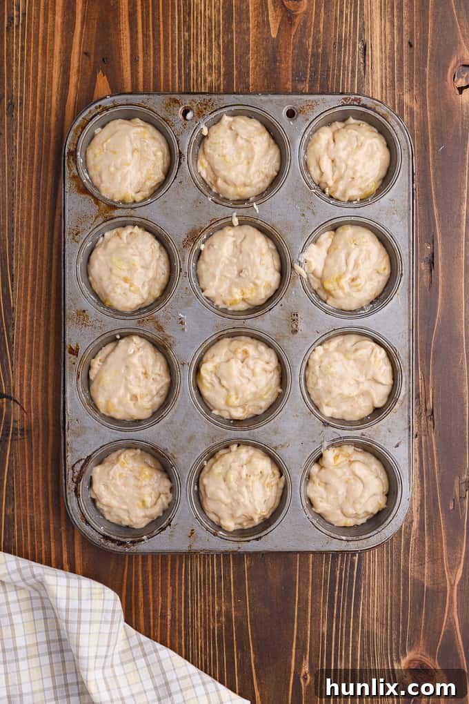 Muffin tin filled with banana muffin batter, topped with streusel, ready for baking.