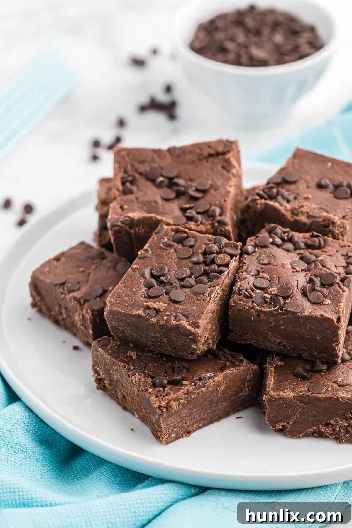 More perfectly cut squares of chocolate cake batter fudge arranged on a white plate, showcasing its rich texture.