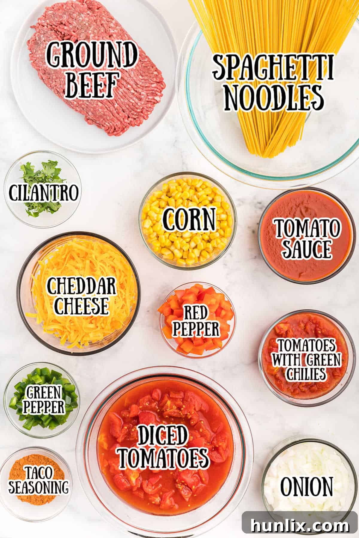A neatly arranged selection of fresh and canned ingredients for Mexican spaghetti on a pristine white kitchen counter.