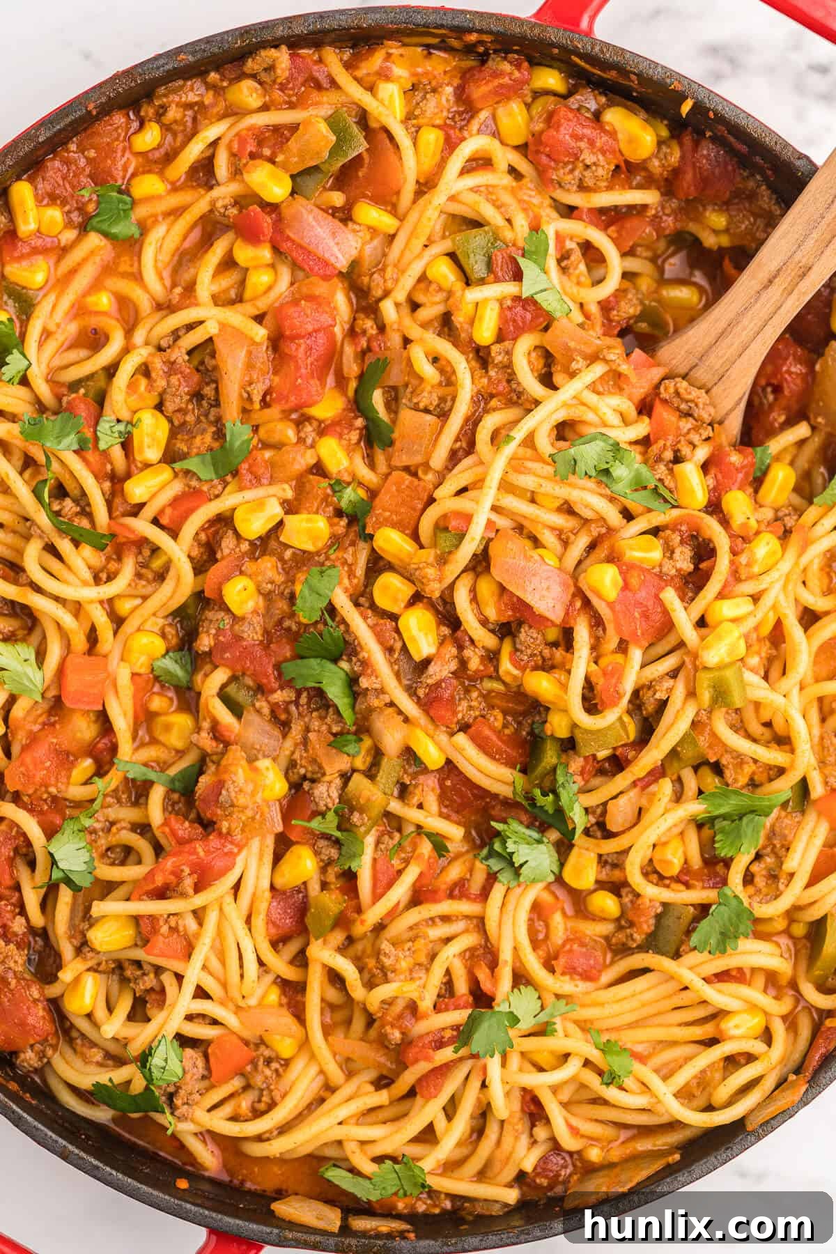 A red pan filled with Mexican spaghetti and a wooden spoon, showcasing the rich texture of the dish.