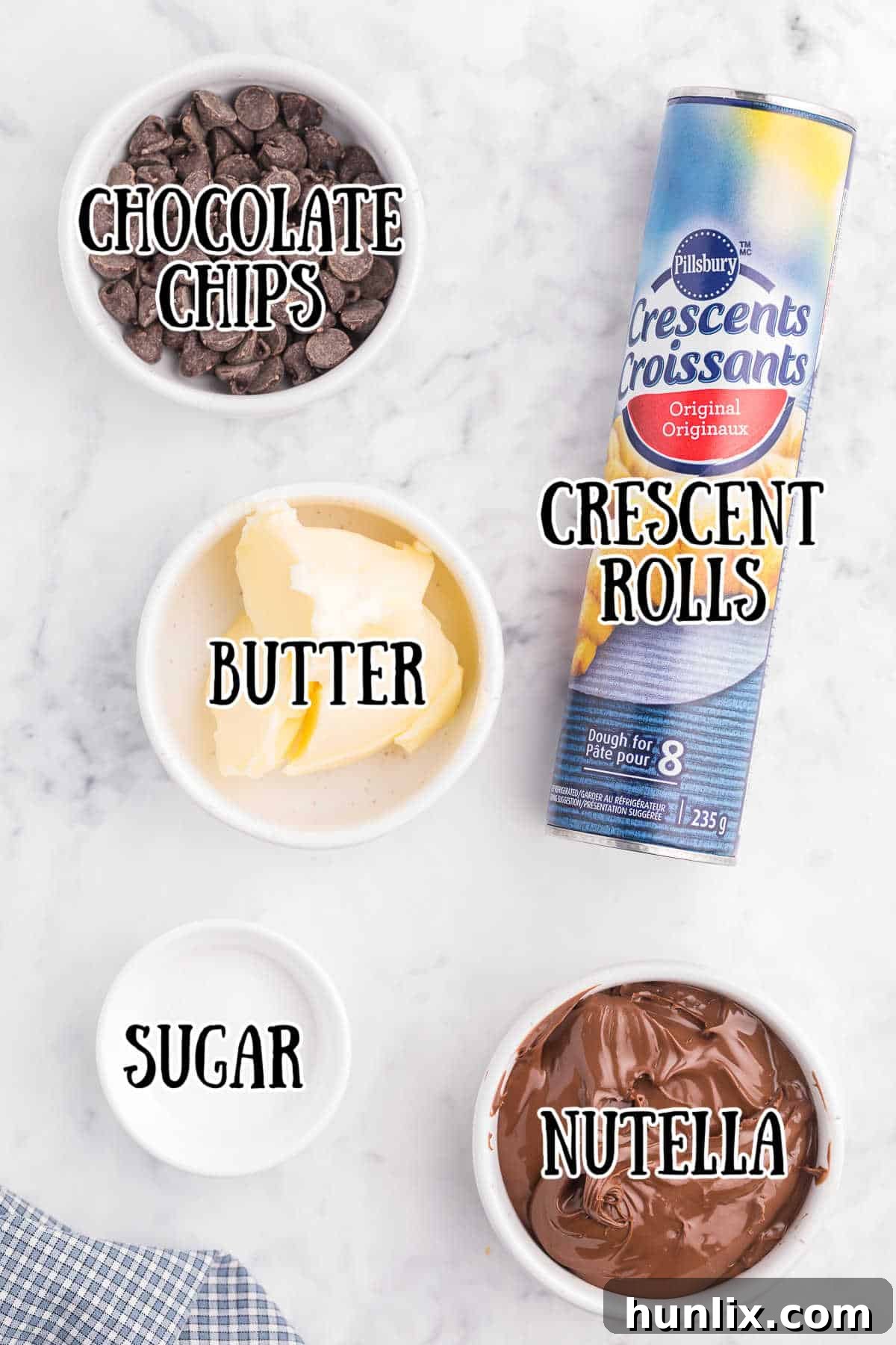 Perfect Air Fryer Chocolate Croissants 3 A flat lay image of all the ingredients for Air Fryer Chocolate Croissants on a white marble counter, including crescent roll dough, Nutella, butter, sugar, chocolate chips, and powdered sugar.