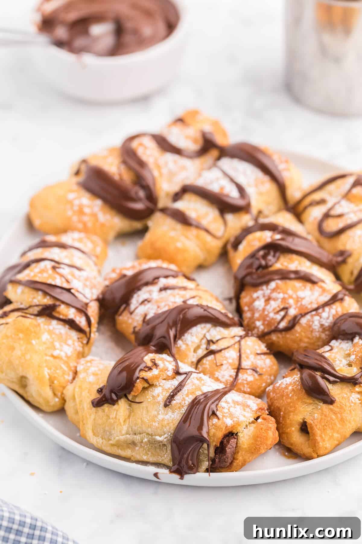 Perfect Air Fryer Chocolate Croissants 8 Air Fryer Chocolate Croissants, freshly baked, dusted with powdered sugar, and drizzled with melted chocolate, served on a white plate.