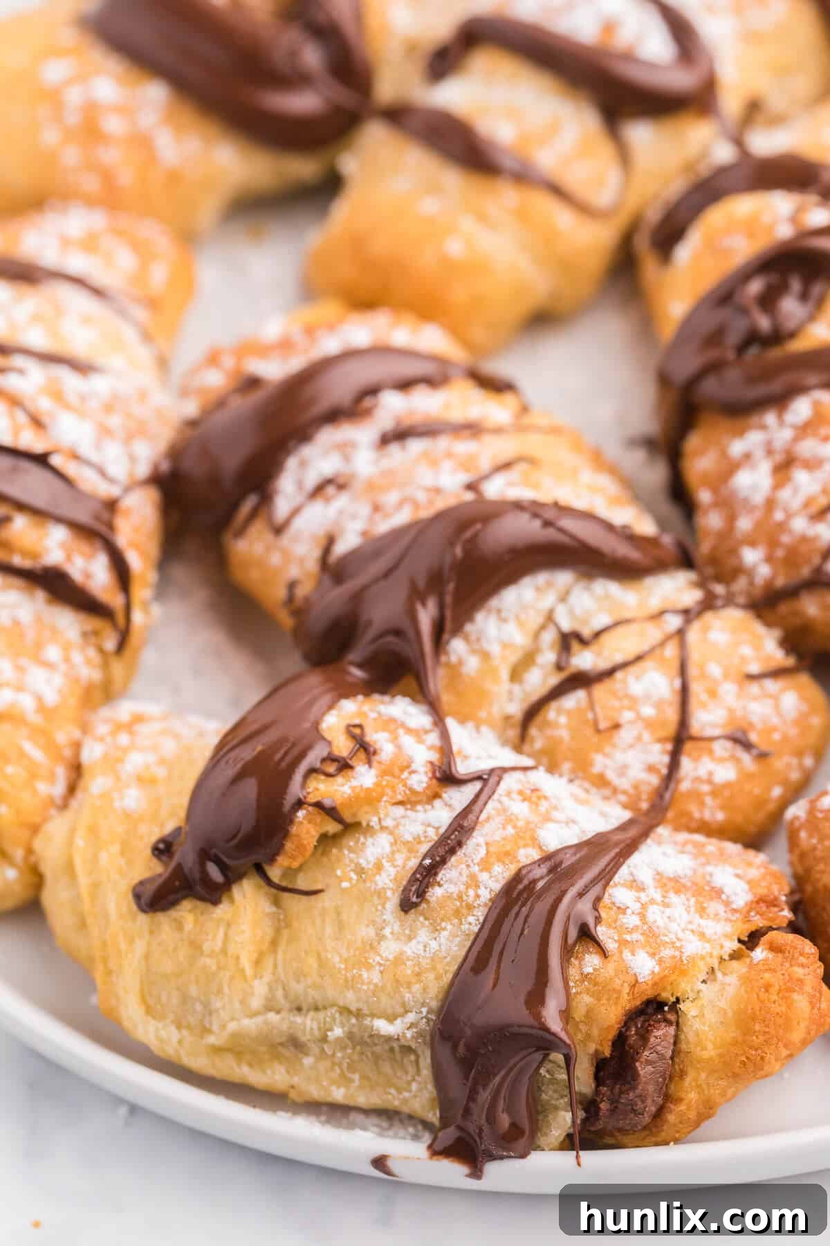 Perfect Air Fryer Chocolate Croissants 9 A close-up of a single Air Fryer Chocolate Crescent Roll on a plate, showing the golden exterior and chocolate drizzle.