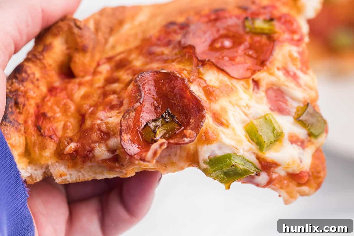 A hand reaching for a slice of freshly cooked air fryer pizza, emphasizing its appetizing appearance.