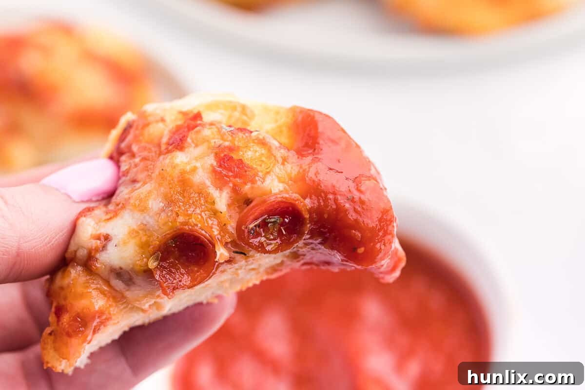 Irresistible Air Fryer Pizza Buns 9 A hand holding an air fryer pizza bun with a bite taken out of it, showing the melted cheese and pepperoni.
