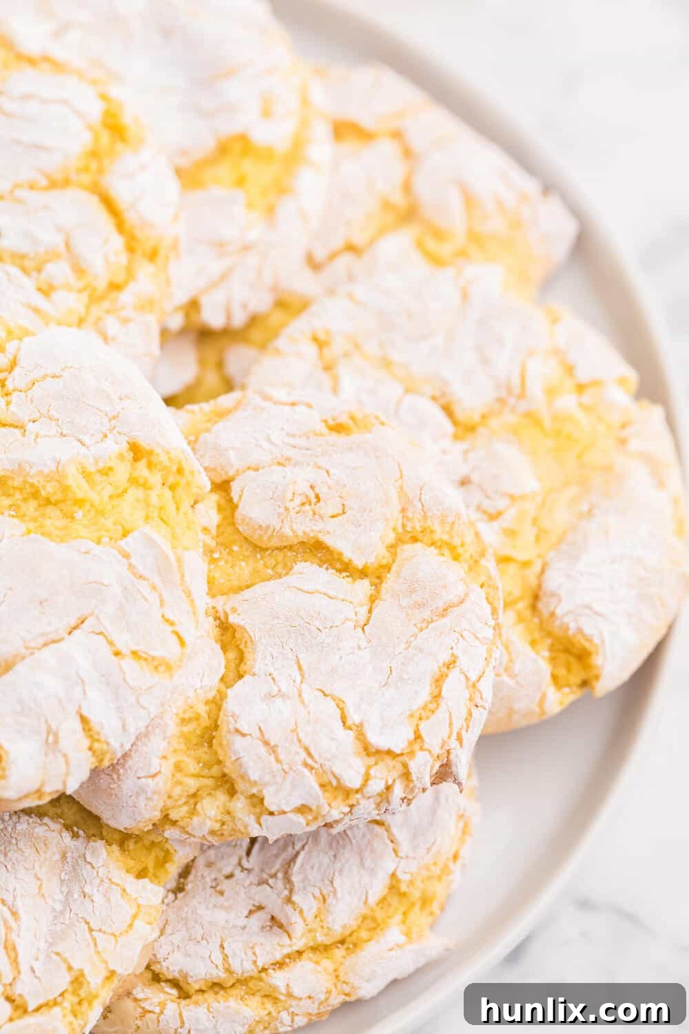 A perfectly baked, crinkled lemon Cool Whip Cookie, dusted with powdered sugar, sitting on a marble surface.