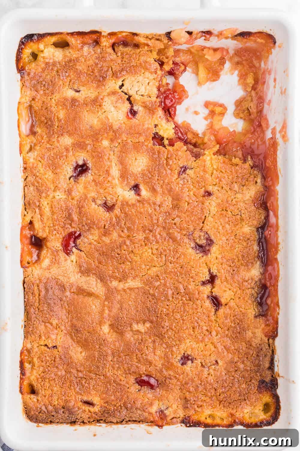 A baked Cherry Pineapple Dump Cake in a 9x13 inch pan with a slice removed, revealing the layers of fruit and cake.