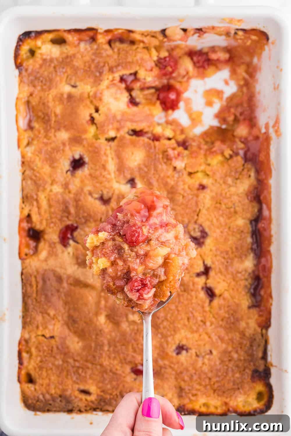 A serving of Cherry Pineapple Dump Cake on a spoon, showing the gooey fruit layers and golden crust.