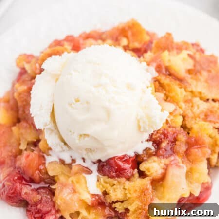 A piece of Cherry Pineapple Dump Cake topped with vanilla ice cream on a plate.