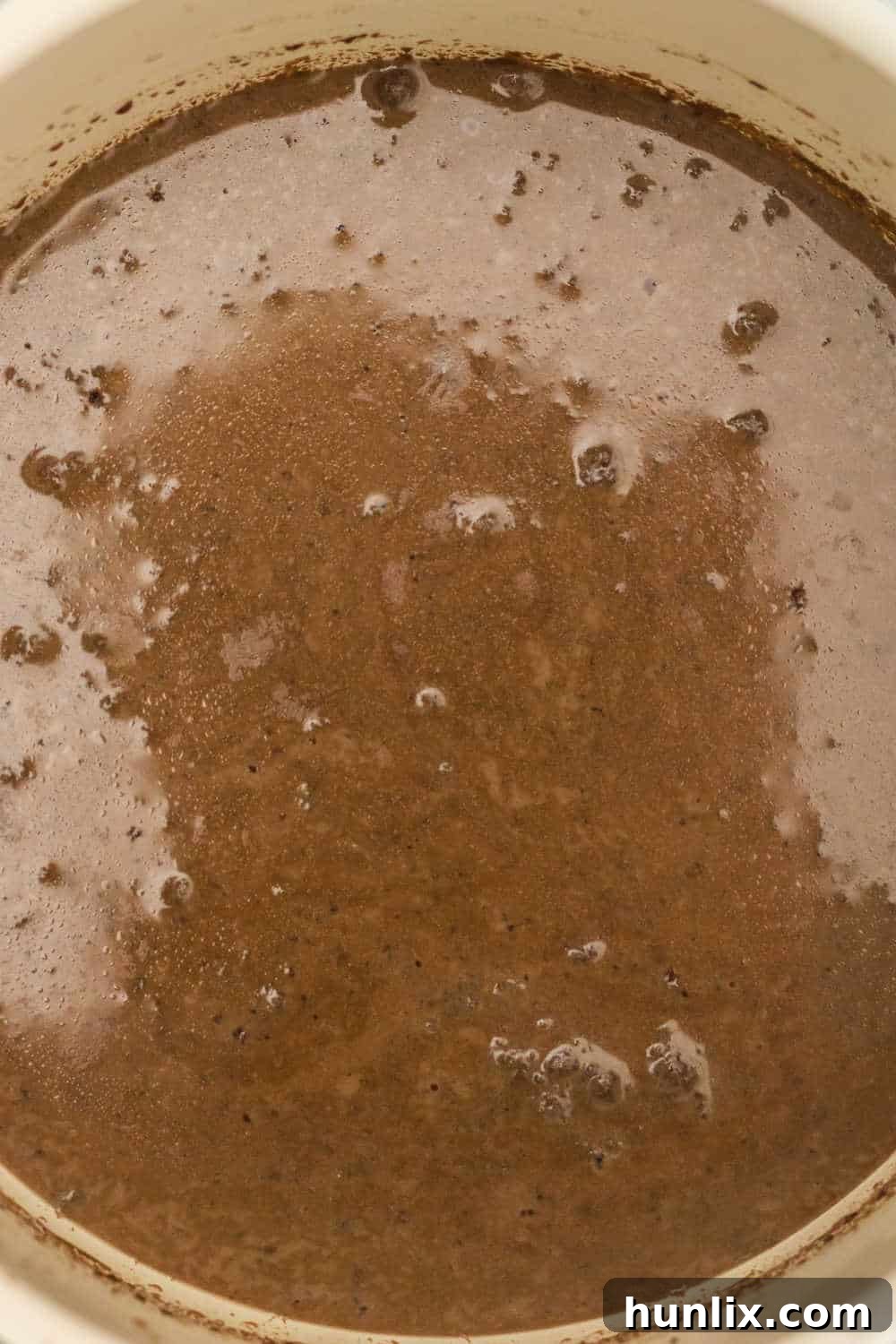 Milk and chocolate chips melting together in a saucepan on a stovetop, as the first step in making cinnamon hot chocolate.