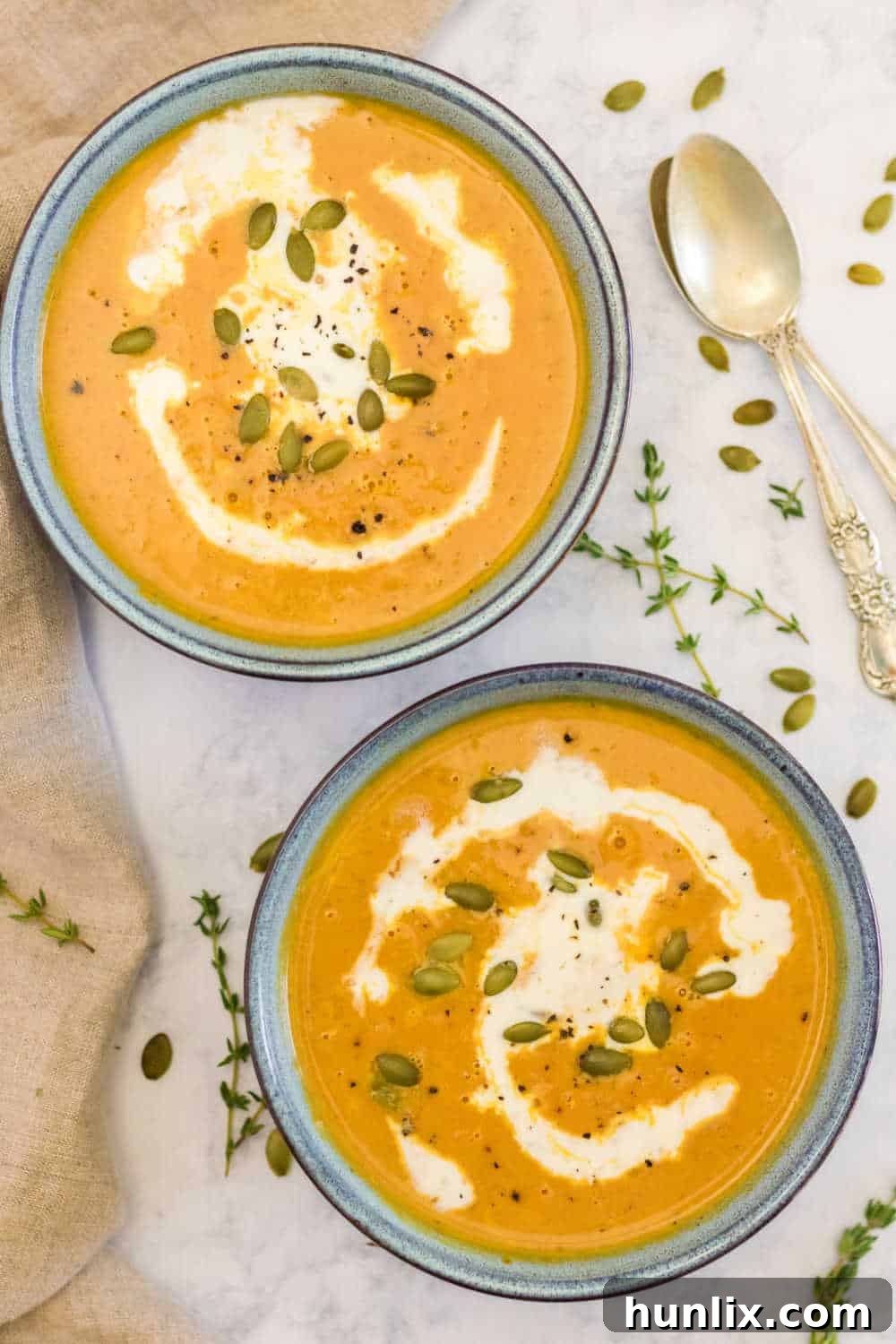 Two bowls of creamy pumpkin soup garnished with fresh herbs and seeds, ready to be served on a rustic wooden table.
