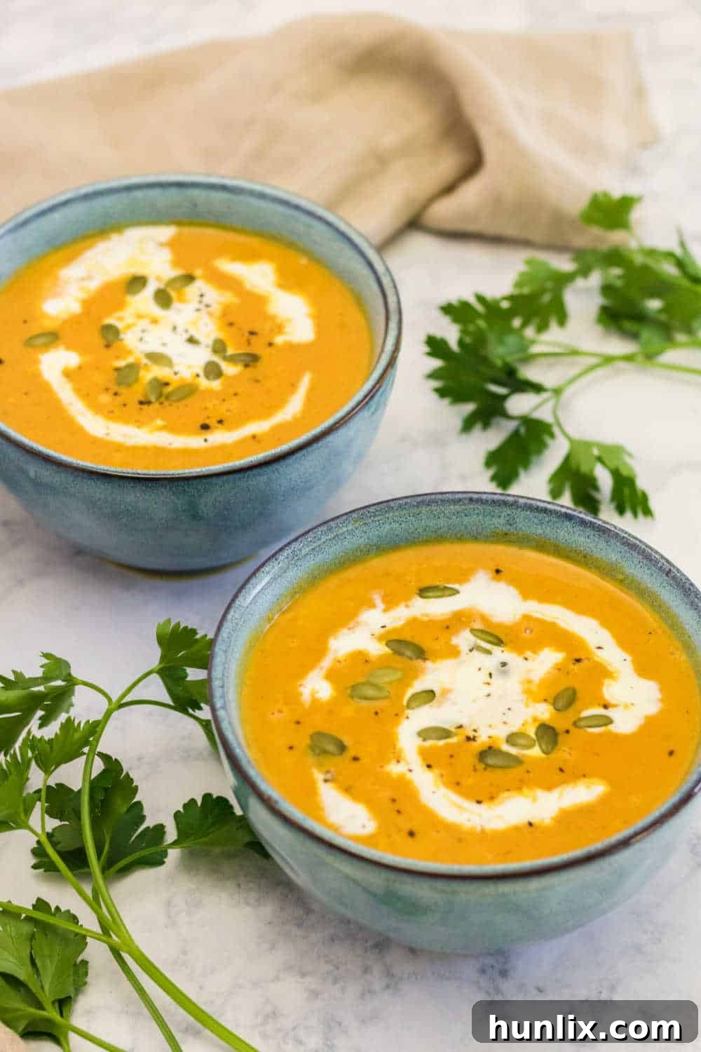 Two cozy bowls of pumpkin soup, one with a spoon, garnished with fresh thyme, on a dark surface, evoking warmth and comfort.