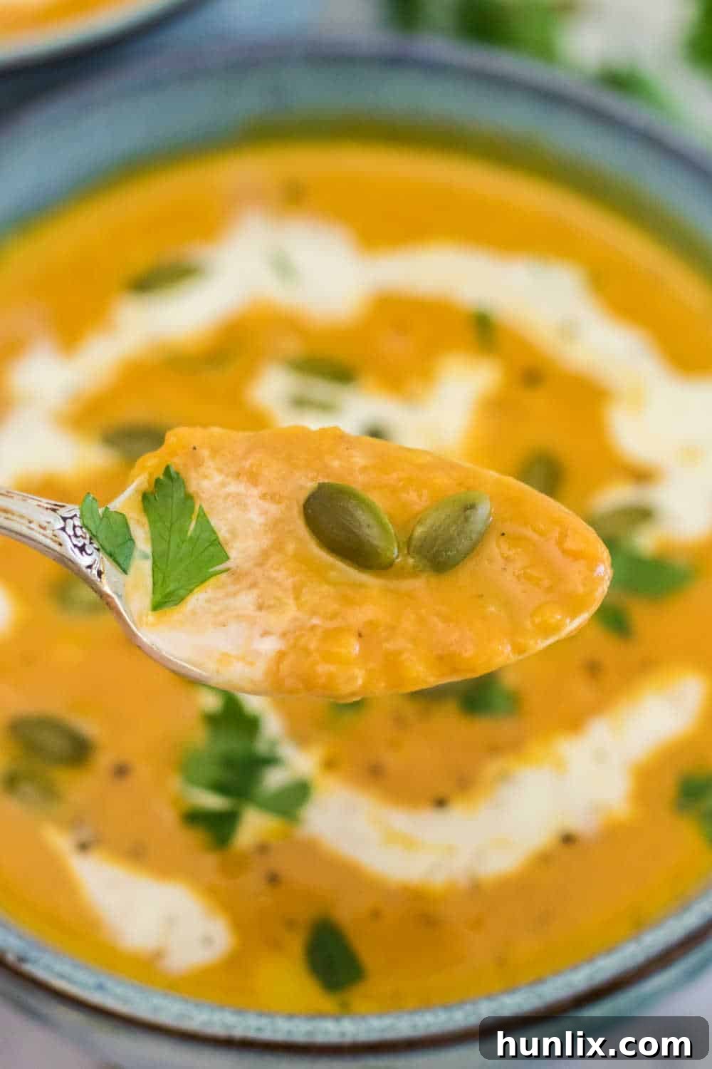 A spoonful of creamy pumpkin soup held over a bowl, highlighting its smooth texture and rich color.