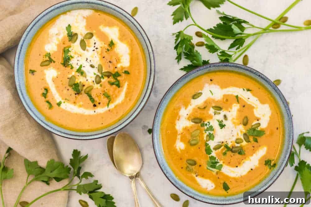 Two bowls of pumpkin soup on a table with a rustic bread board and fresh herbs, showcasing a complete meal setting.