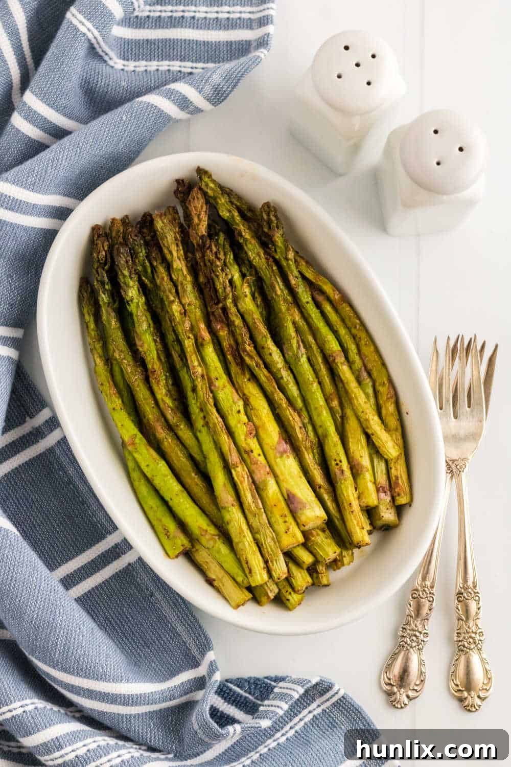 Air fryer asparagus in a white casserole dish, garnished with fresh lemon slices.