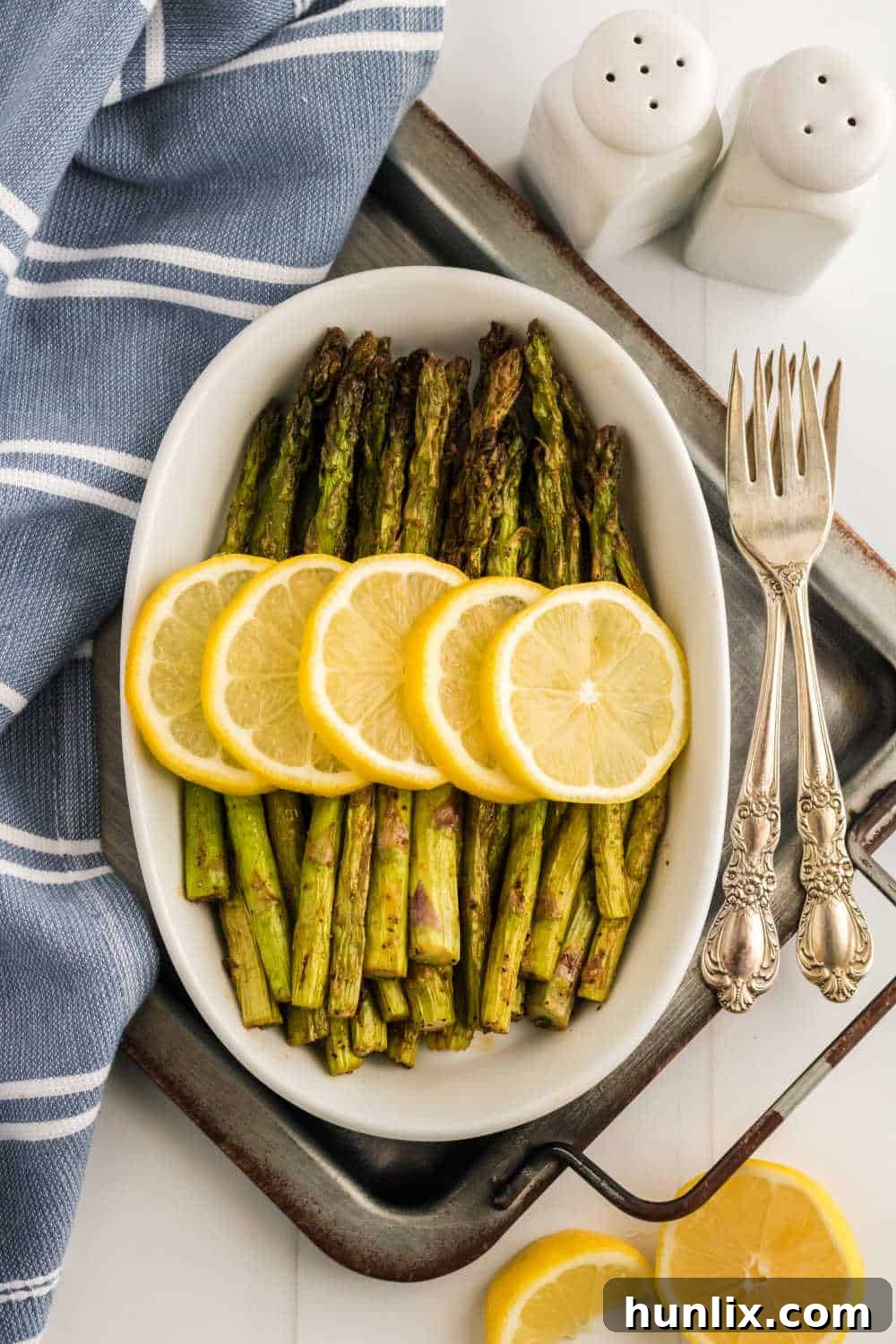 The air fryer asparagus recipe topped with sliced lemon in a white casserole dish.