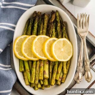 The air fryer asparagus recipe in a white dish topped with lemon slices.
