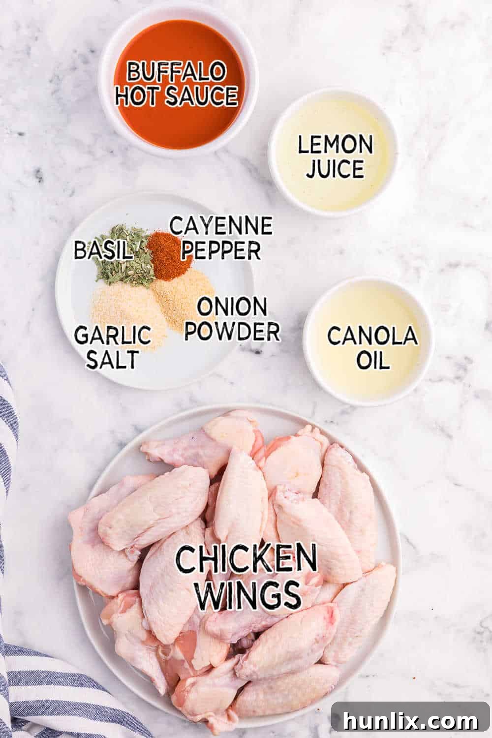 A collection of fresh ingredients for Air Fryer Buffalo Chicken Wings laid out on a marble counter, including chicken wings, various spices, oil, and lemon.