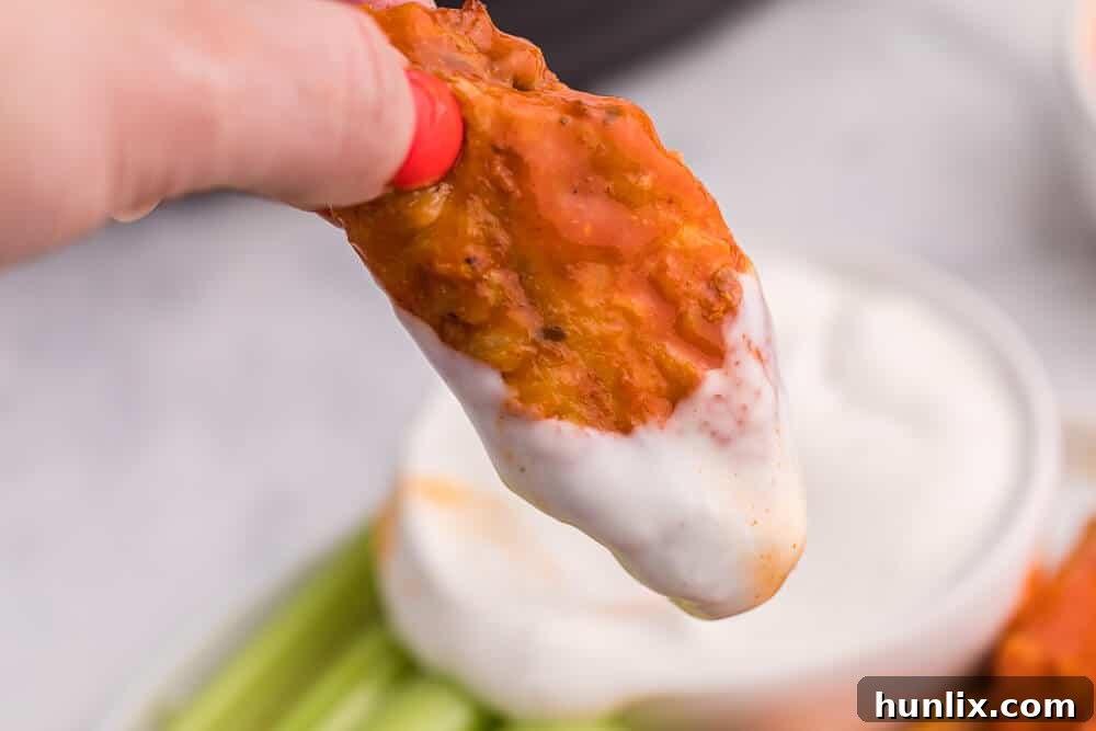 A hand holding a perfectly sauced Air Fryer Buffalo Chicken Wing, dipped in rich ranch dressing, ready to be enjoyed.