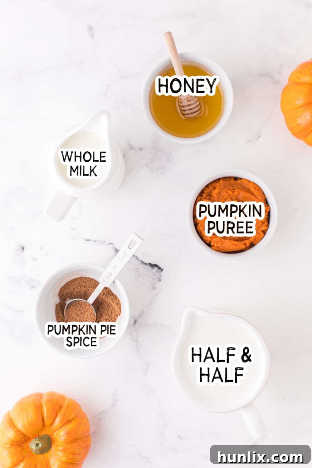 Velvet Pumpkin Coffee Swirl 3 A collection of ingredients for homemade pumpkin spice creamer, including half and half, whole milk, pumpkin puree, honey, and pumpkin pie spice, neatly arranged on a white marble countertop.