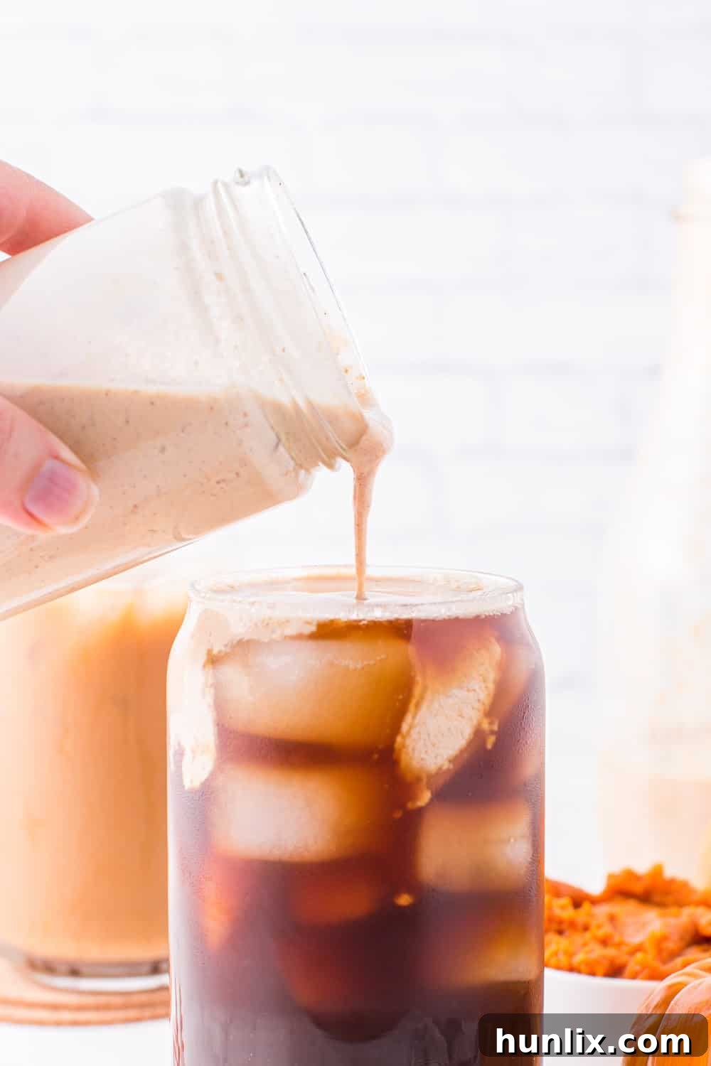 Velvet Pumpkin Coffee Swirl 6 Homemade pumpkin spice creamer being poured into a glass of iced coffee, showing its creamy texture.