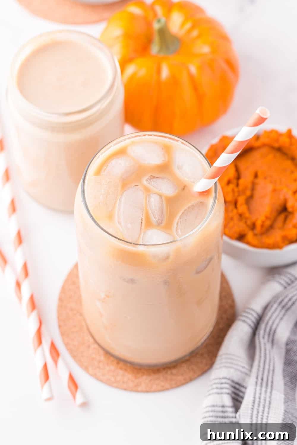Velvet Pumpkin Coffee Swirl 9 A glass jar with iced coffee and a straw, featuring homemade pumpkin spice creamer creating a beautiful swirl.