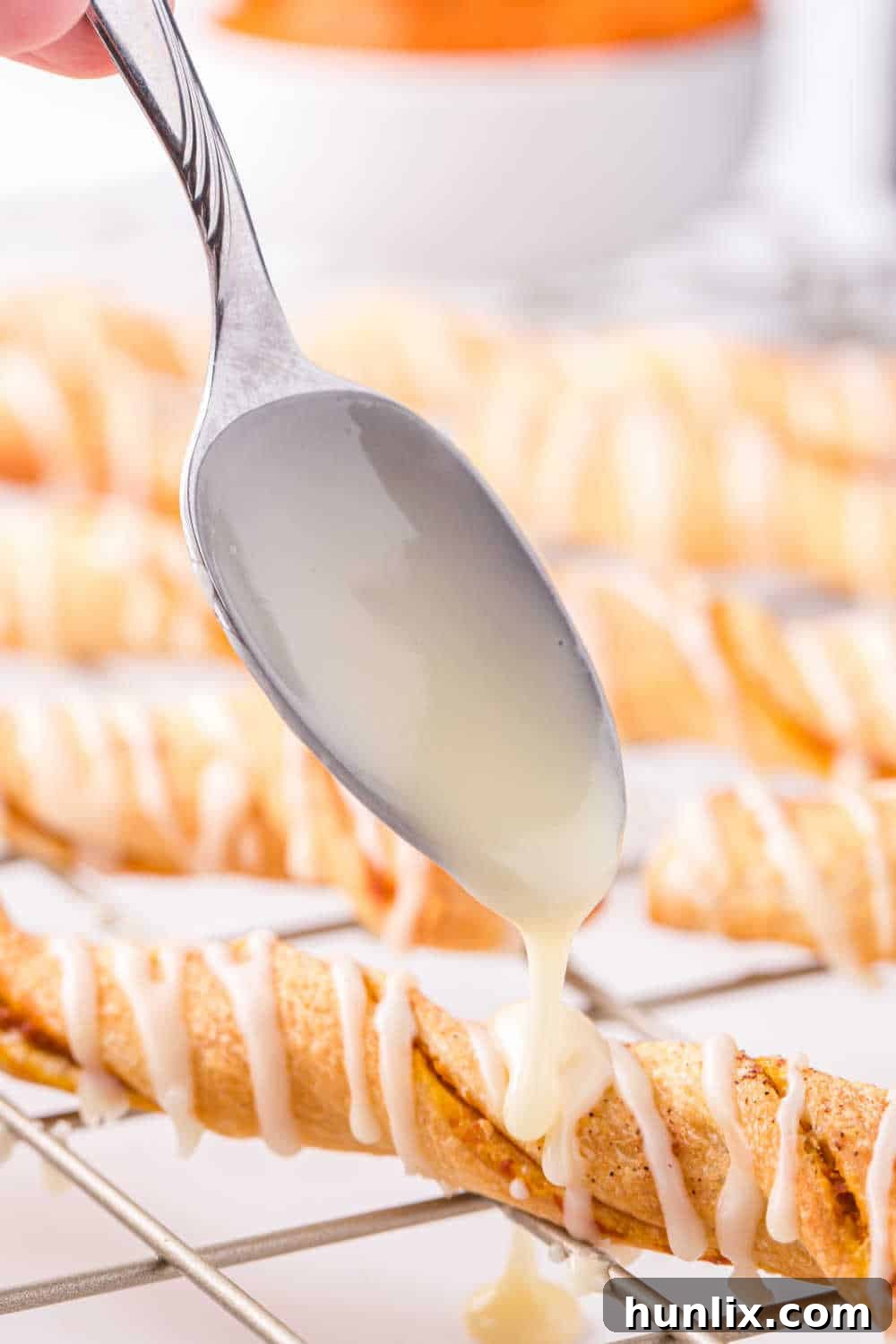 A beautifully composed shot of the finished Air Fryer Pumpkin Pie Twists, with a spoon elegantly drizzling the sweet orange glaze over them.
