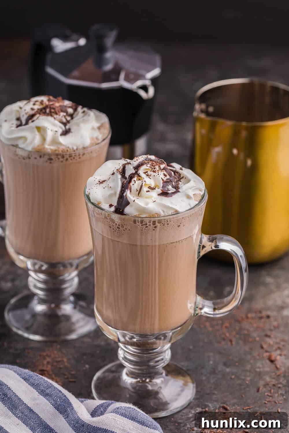 Two mugs of mocha latte with an espresso maker and a milk frothing pitcher, tempting on a cold day.