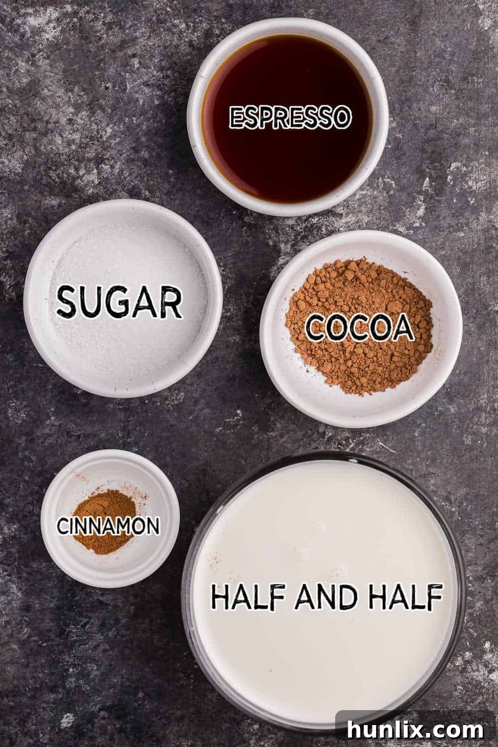 Ingredients for mocha latte laid out on a dark background, including half and half, cocoa powder, sugar, cinnamon, and espresso.