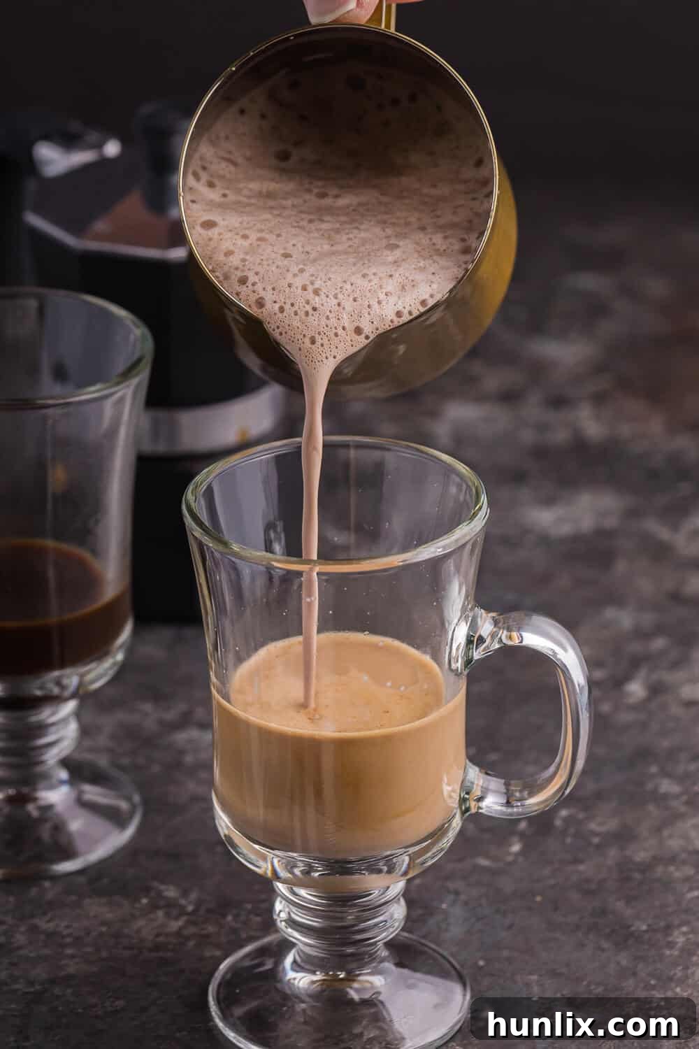 Pouring the frothed chocolate mixture into a mug of espresso to complete the mocha latte.