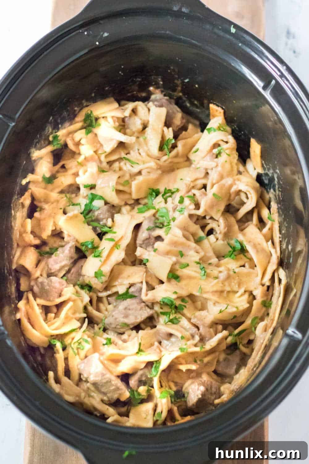 Tender beef and rich egg noodles simmering in a black slow cooker, ready to be served.