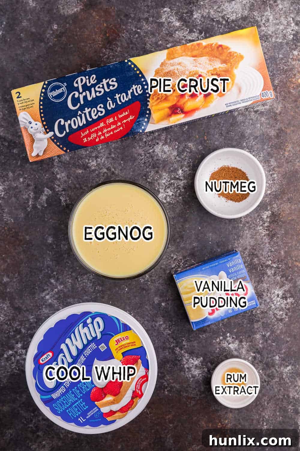 Key ingredients for eggnog pie laid out on a dark surface.