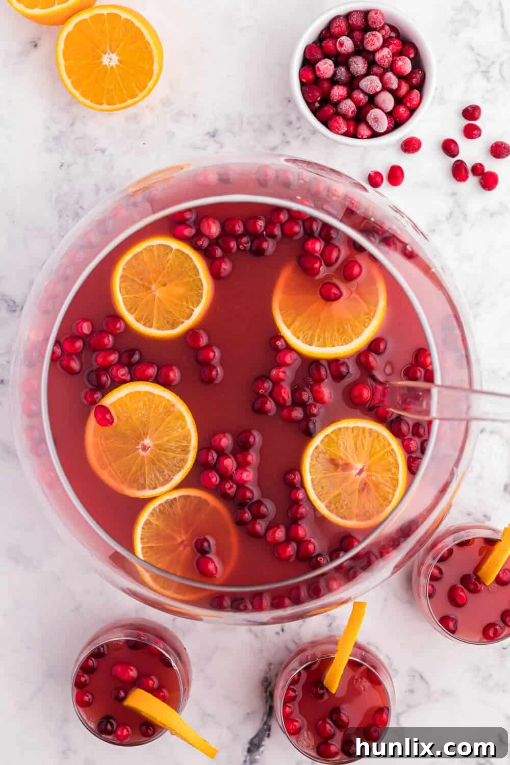 Christmas punch in a punch bowl with glasses and a ladle, garnished with fresh orange slices and frozen cranberries.
