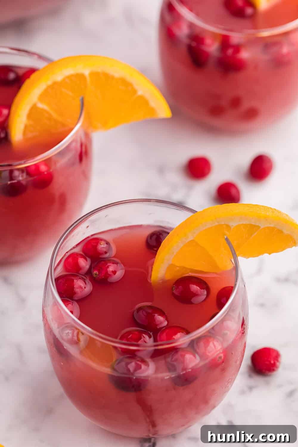 A single glass of Christmas punch, showcasing the vibrant red drink with an orange slice and frozen cranberries as garnish.