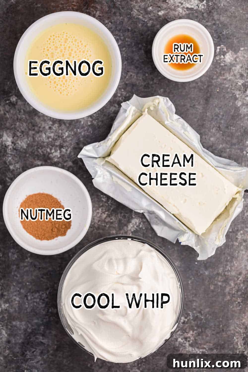 A collection of ingredients laid out, including cream cheese, eggnog, nutmeg, rum extract, and Cool Whip, ready for making Eggnog Dip.