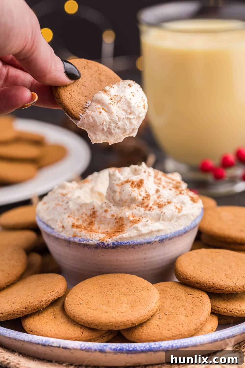 A hand holding a gingersnap cookie generously coated with fluffy Eggnog Dip, highlighting its creamy texture.