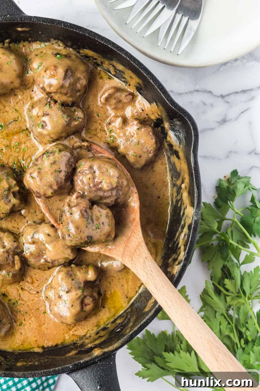 Traditional Swedish Meatballs 9 Swedish meatballs in a cast iron skillet with a wooden serving spoon, ready to be dished out.