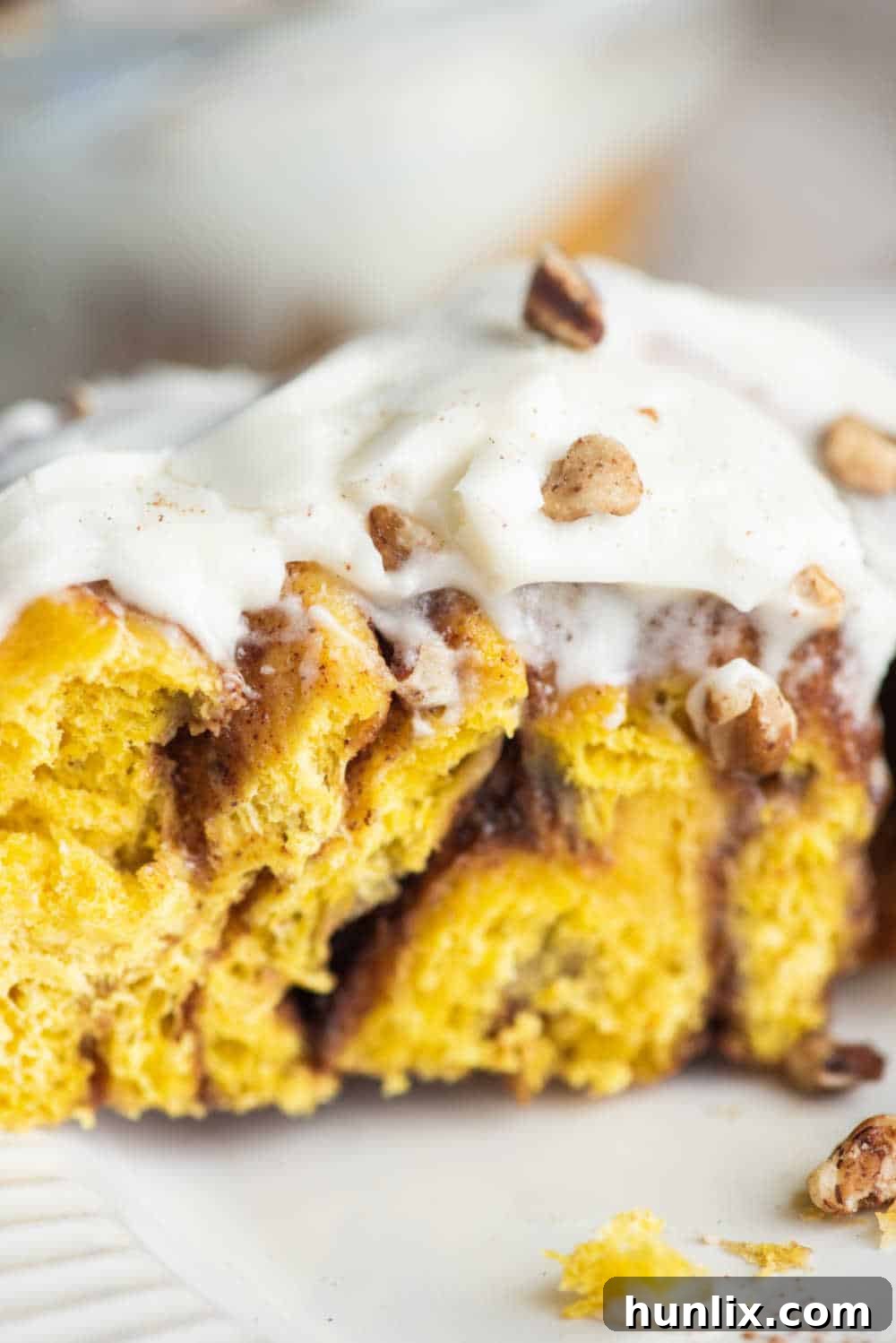Pumpkin Spice Cinnamon Swirls 11 A close-up of a pumpkin cinnamon roll on a white plate, garnished with toasted nuts